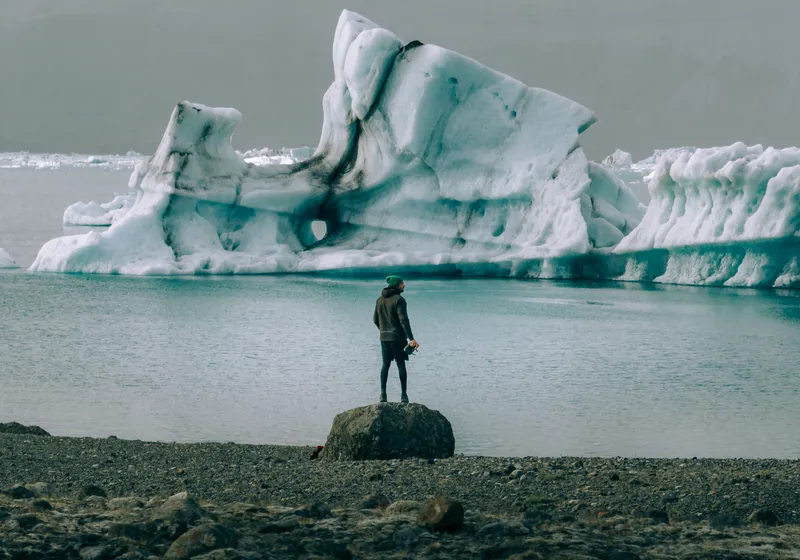 A person standing by a glacier lagoon full of icebergs