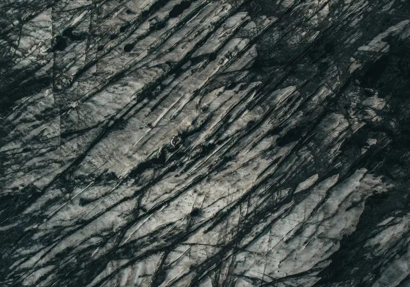 A glacier from above, white ice streaked with black volcanic sand