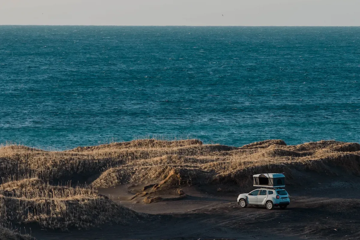 Campervan parked on Iceland’s coastline with ocean views, showing off-road dunes and open landscape during a road trip adventure.