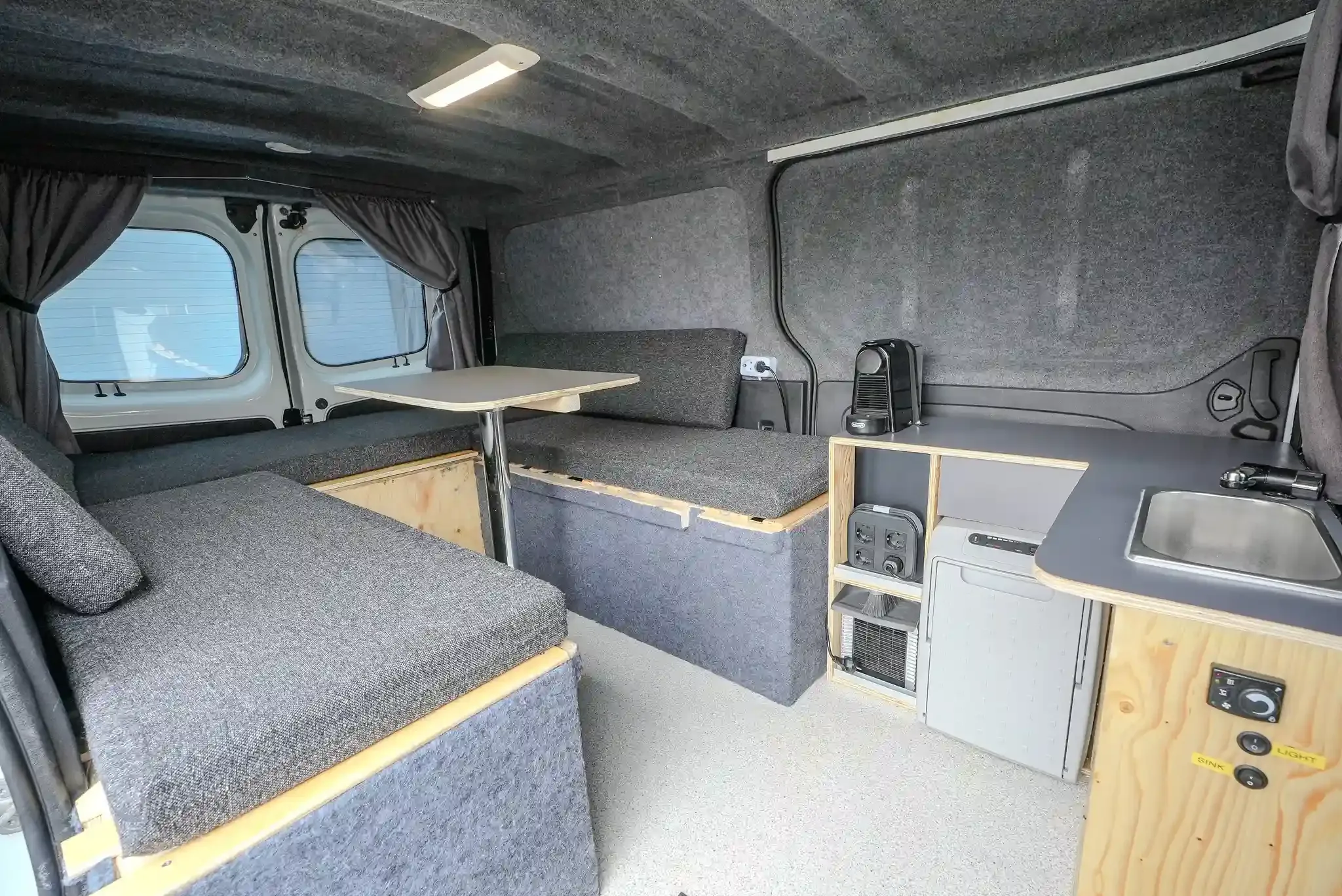 Interior of Trafic 3 campervan with sink, fridge, sofa area, heating controls, and Nespresso coffee machine