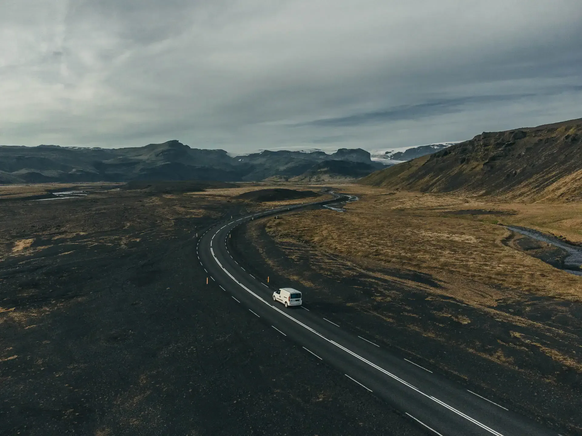 Small campervan driving along a winding road through volcanic landscapes in Iceland