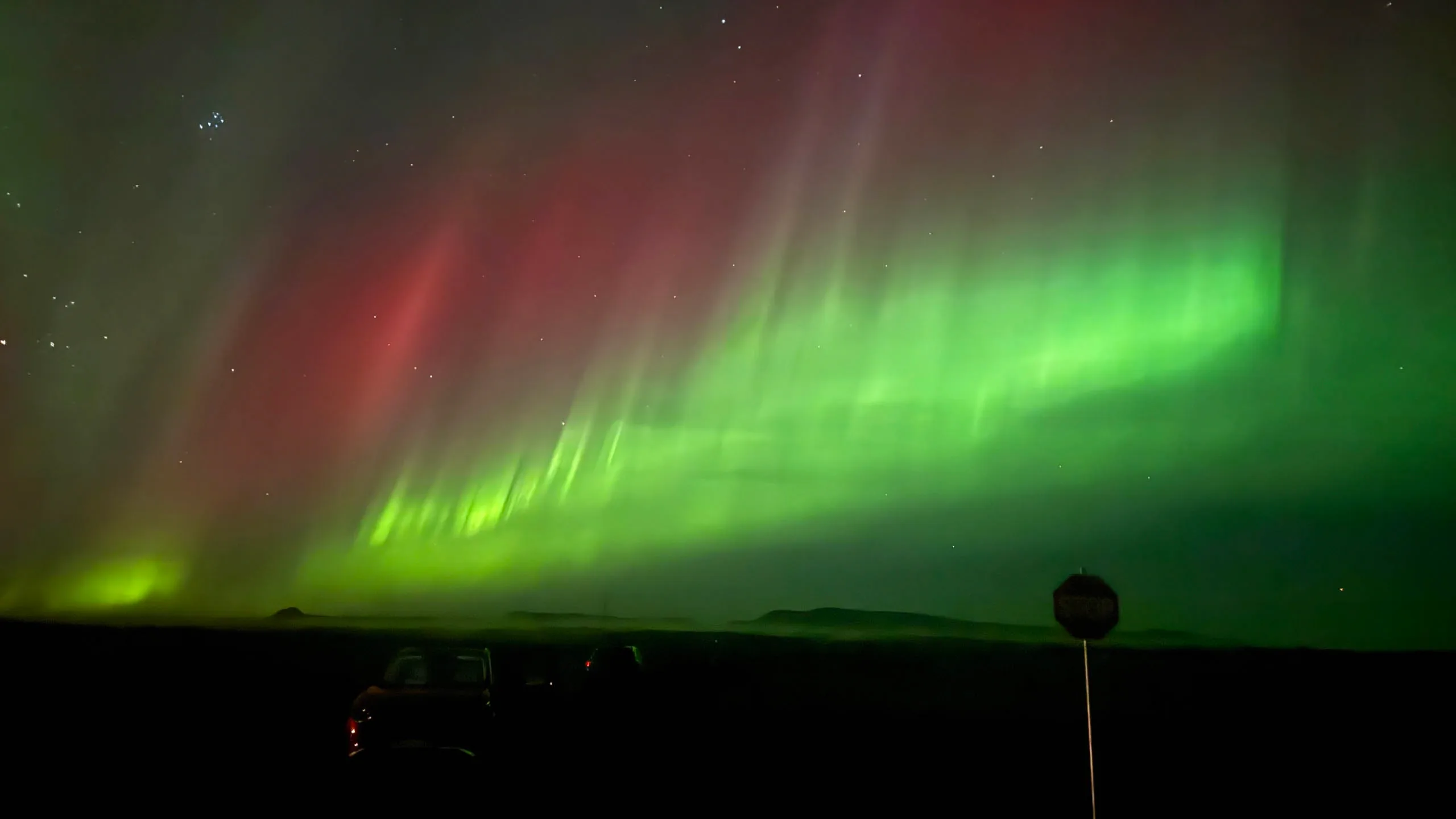 Swirling green Northern Lights in Iceland stretching across the sky above the moonlit coastline and distant mountains. 