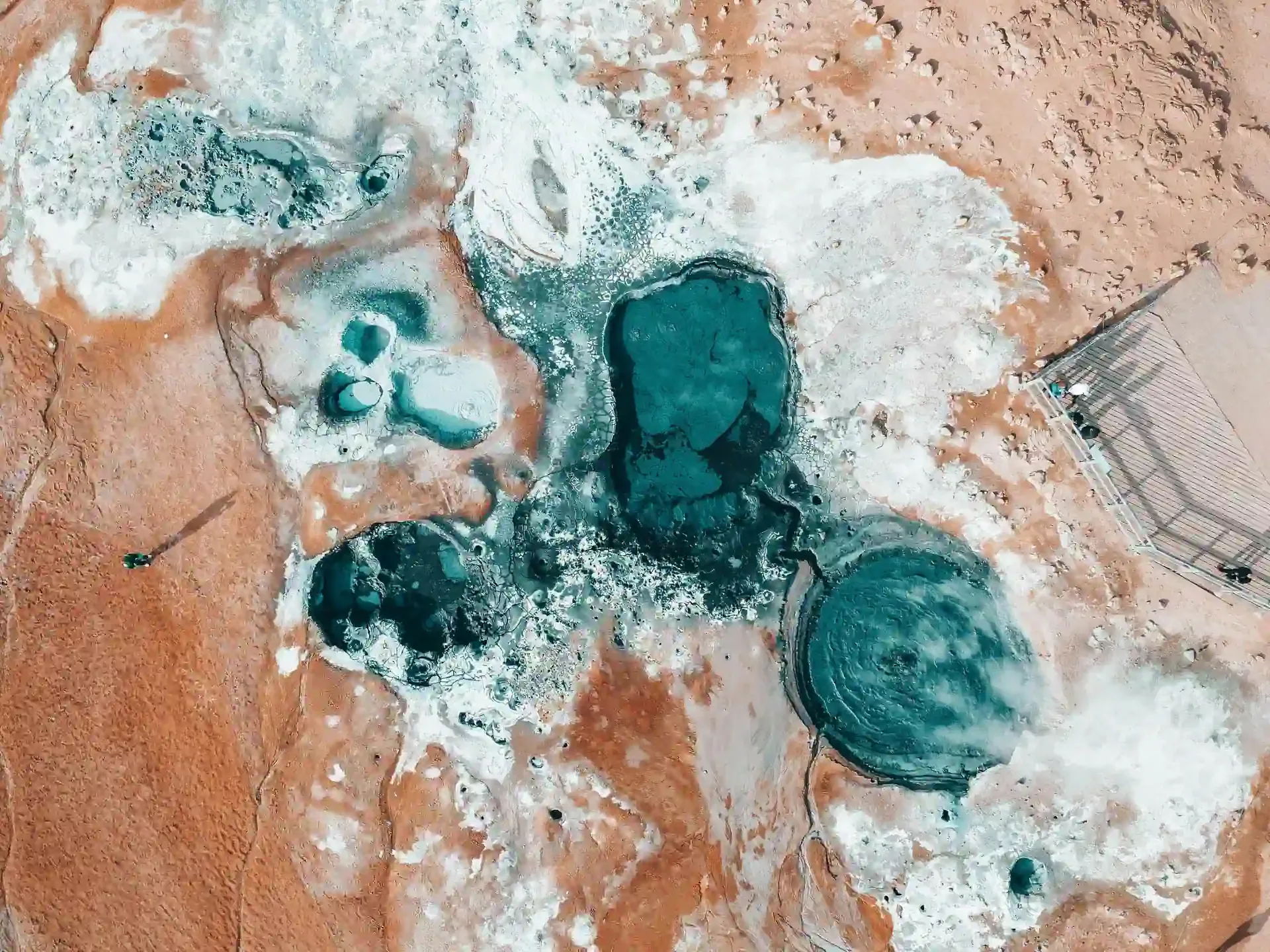 Aerial view of Icelandic geothermal hot pools with turquoise and teal mineral water surrounded by white mineral deposits and rust-colored earth