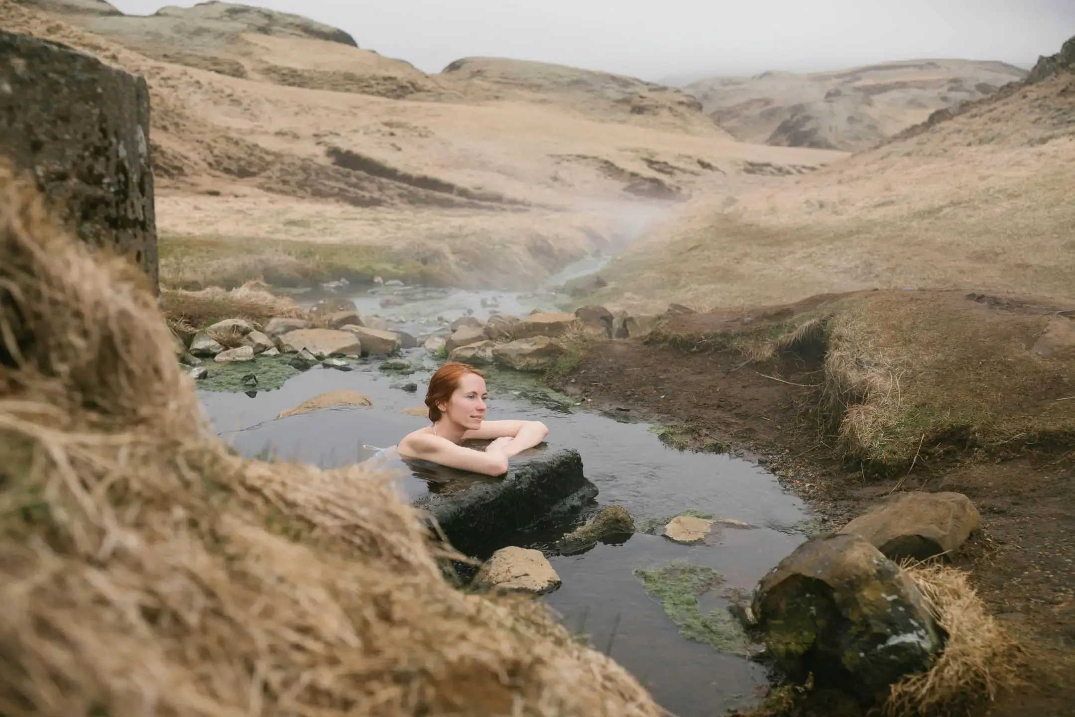 Outdoor geothermal swimming pool in Iceland with steam rising from warm water and mountains in the background
