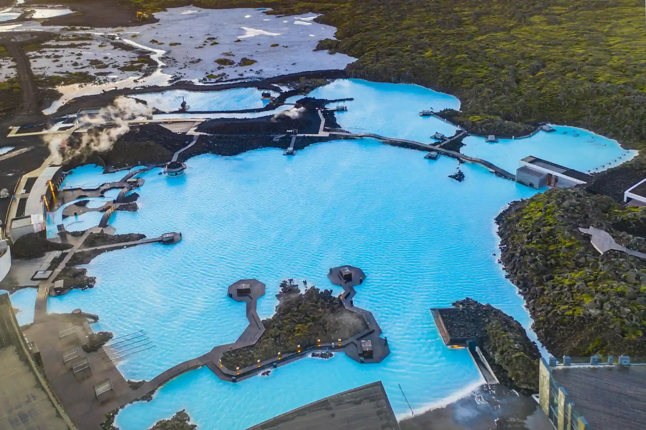 Aerial view of Icelandic geothermal hot pools with turquoise and teal mineral water surrounded by white mineral deposits and rust-colored earth