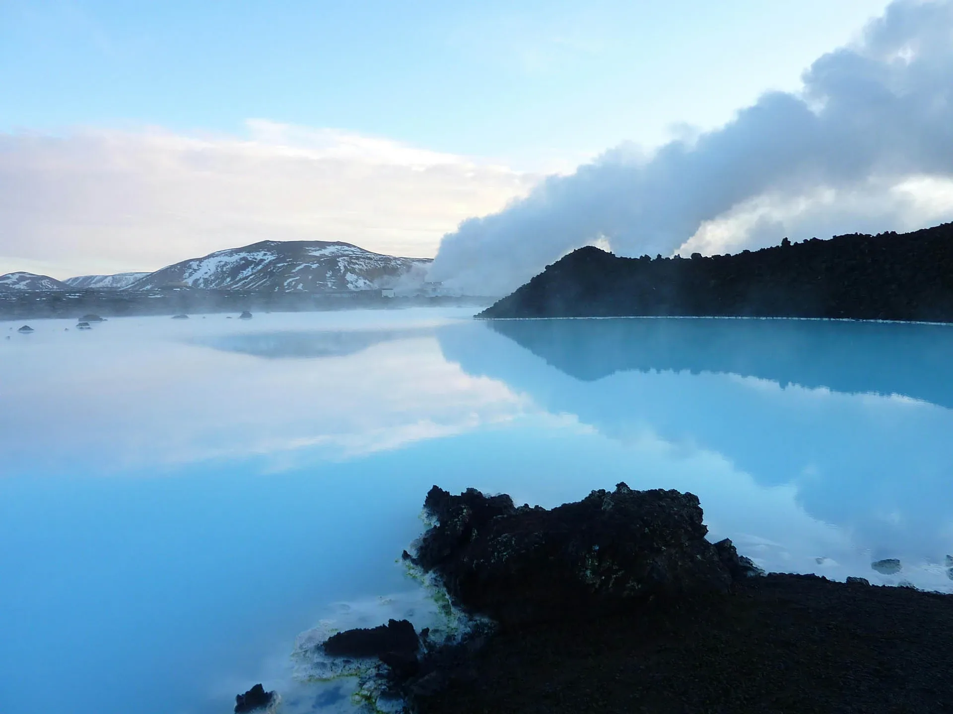 celand Blue Lagoon geothermal spa with turquoise water, steam, snow-capped mountains, and black lava formations