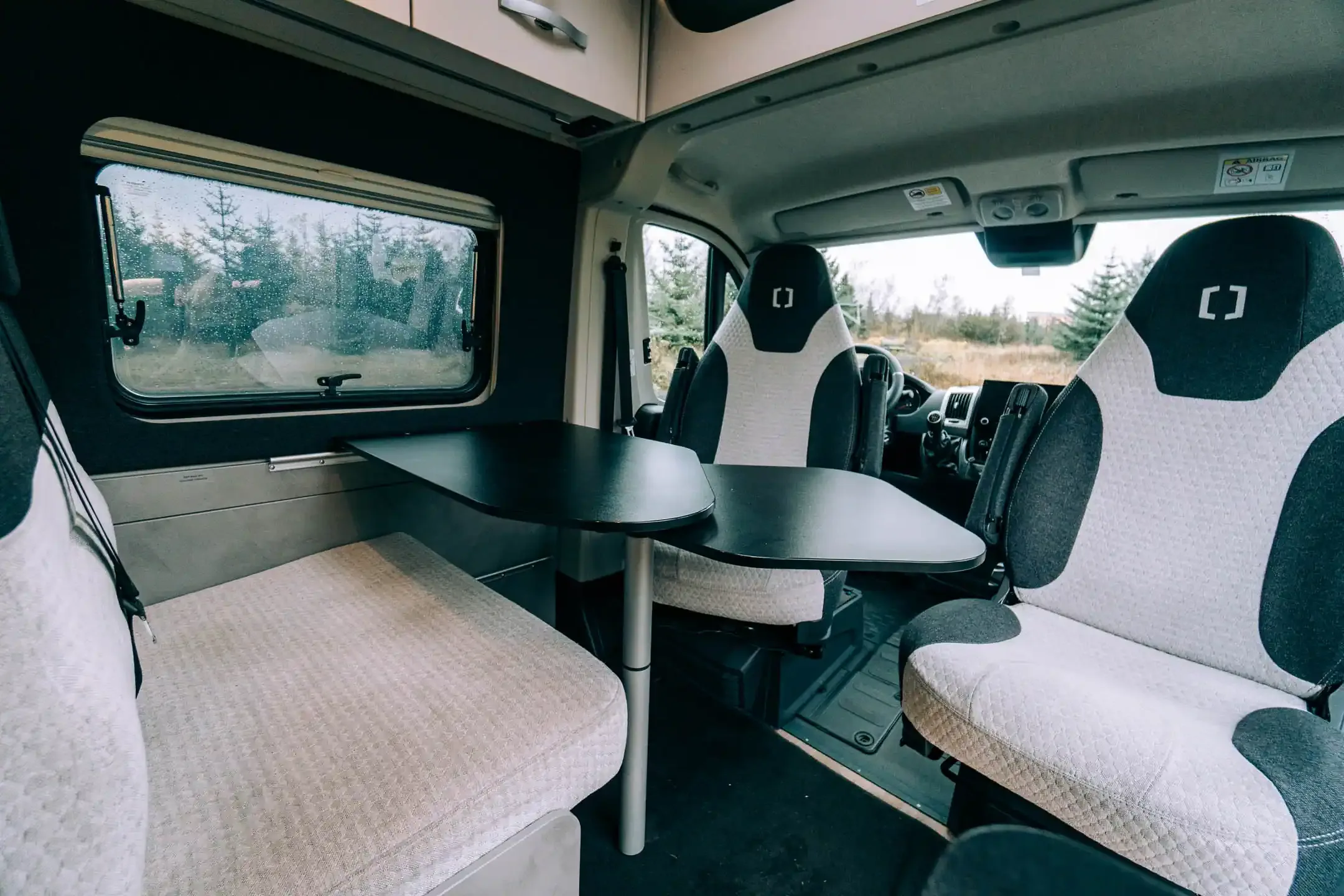 Modern campervan interior with swivel front seats, dining table, and kitchenette, designed for comfortable road trips in Iceland.