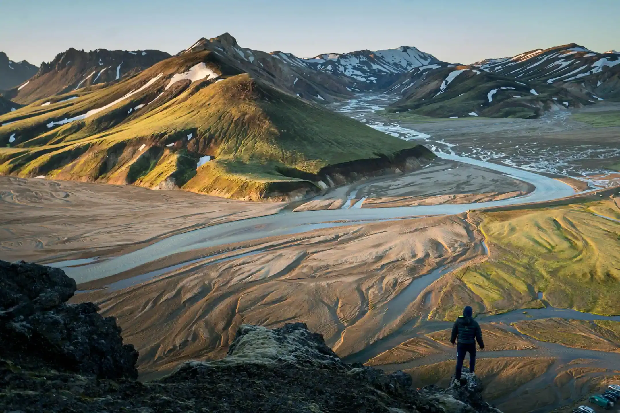 Hiker overlooking braided glacial rivers in the Icelandic Highlands near Landmannalaugar, illustrating the terrain where travelers cross rivers in Iceland on F-roads.