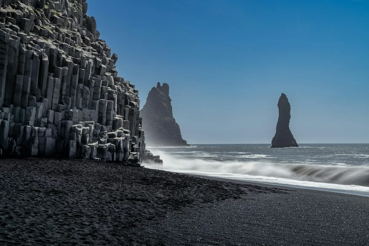 Basalt column cliffs and Reynisdrangar sea stacks at Reynisfjara Black Sand Beach with waves crashing along the volcanic shoreline in South Iceland.