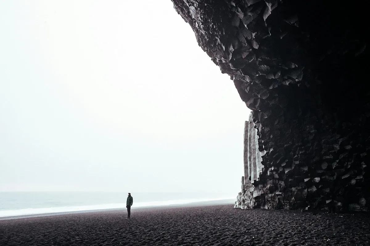 View from inside the basalt cave, looking out toward the Reynisdrangar sea stacks and the Atlantic Ocean under cloudy skies.