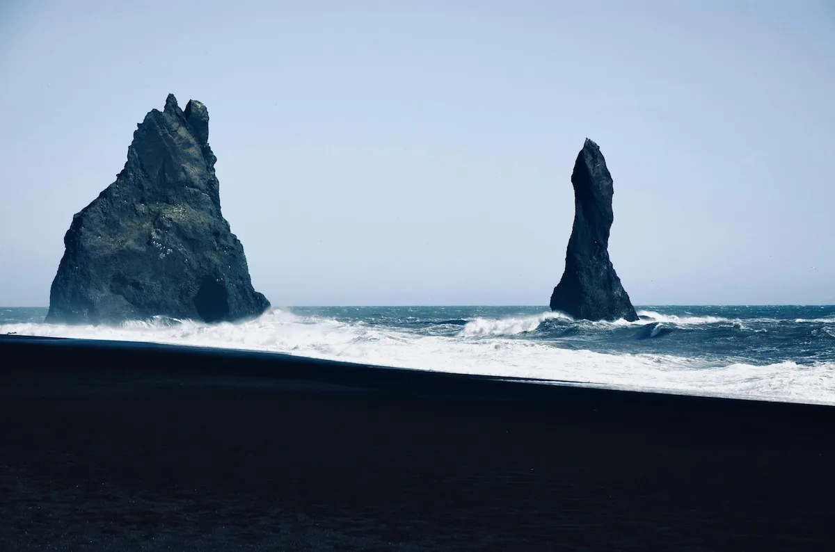 Reynisdrangar sea stacks rising from the Atlantic Ocean at Reynisfjara Black Sand Beach, with waves crashing against the volcanic coastline in South Iceland.