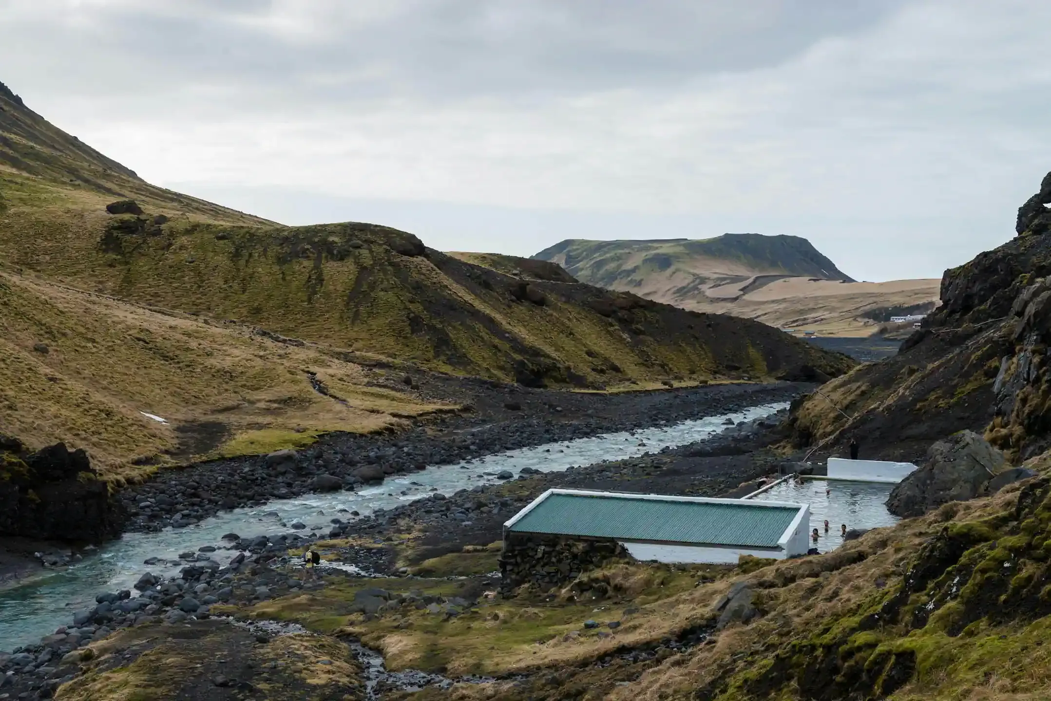 Seljavallalaug geothermal pool in a remote Icelandic valley, one of the top free things to do in Iceland with mountains, a river and hikers in the landscape