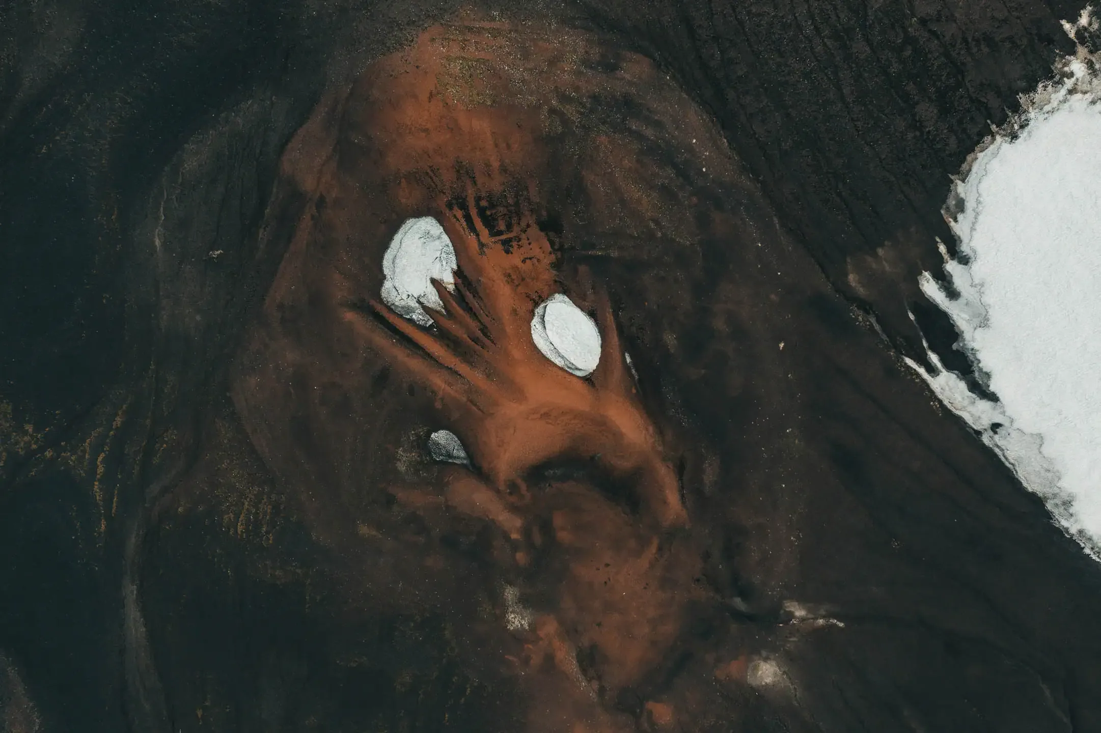 Abstract aerial view of Iceland’s volcanic highlands showing deep black ash fields, rust colored ridges and pockets of melting white snow.