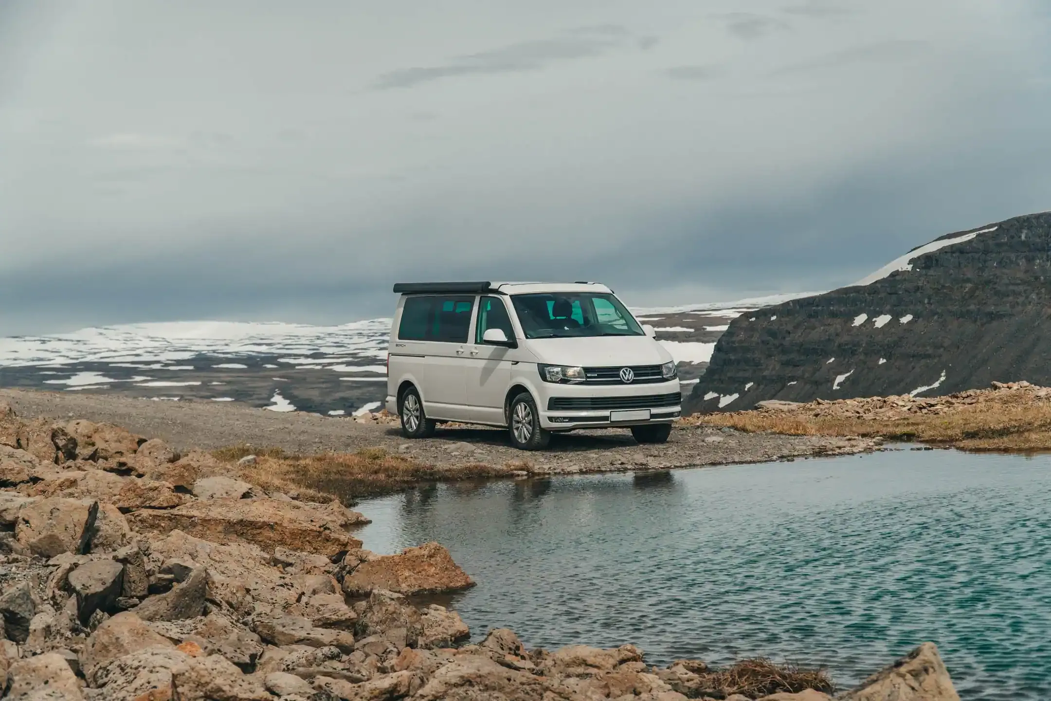 Campervan parked beside a mountain lake in Iceland’s highlands with snow patches and rocky terrain
