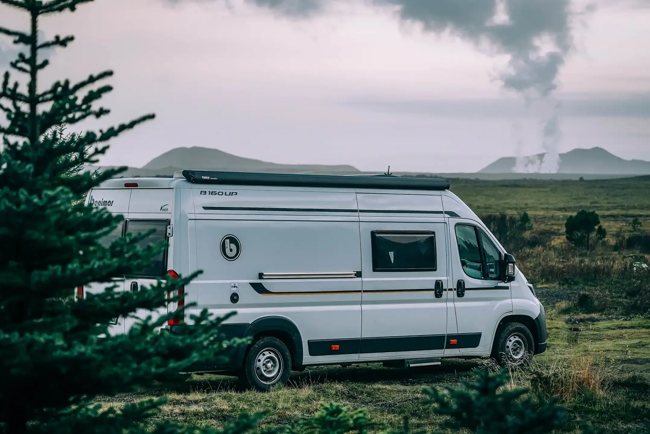 Family campervan Iceland parked in green countryside with steam rising from distant hills on a family road trip