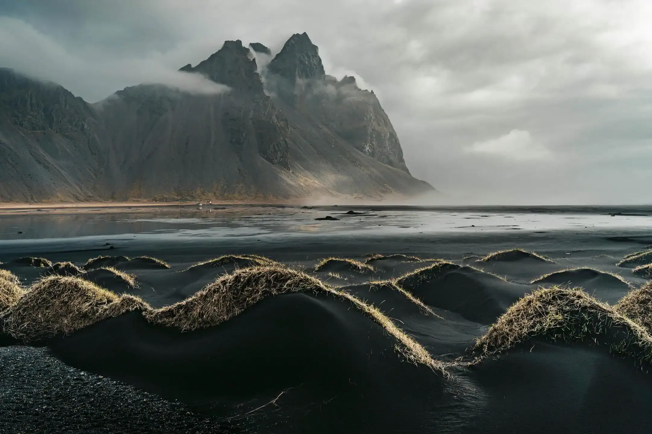 Moody coastal view of Vestrahorn mountain with mist and black sand dunes in East Iceland.