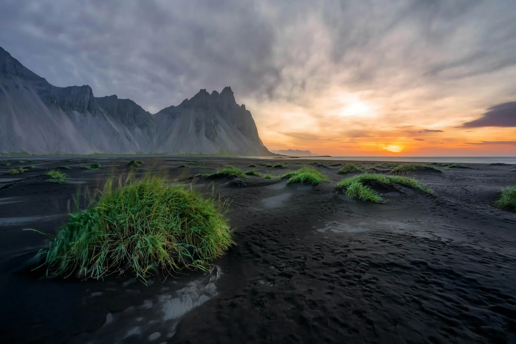 Black sand dunes with green grass in front of Vestrahorn mountain at sunrise in East Iceland