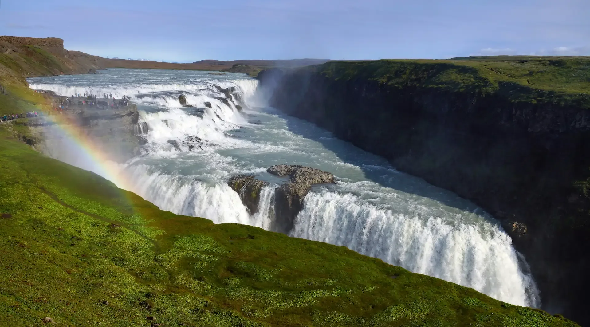 Gullfoss waterfall cascading through a green canyon with a rainbow in the mist.