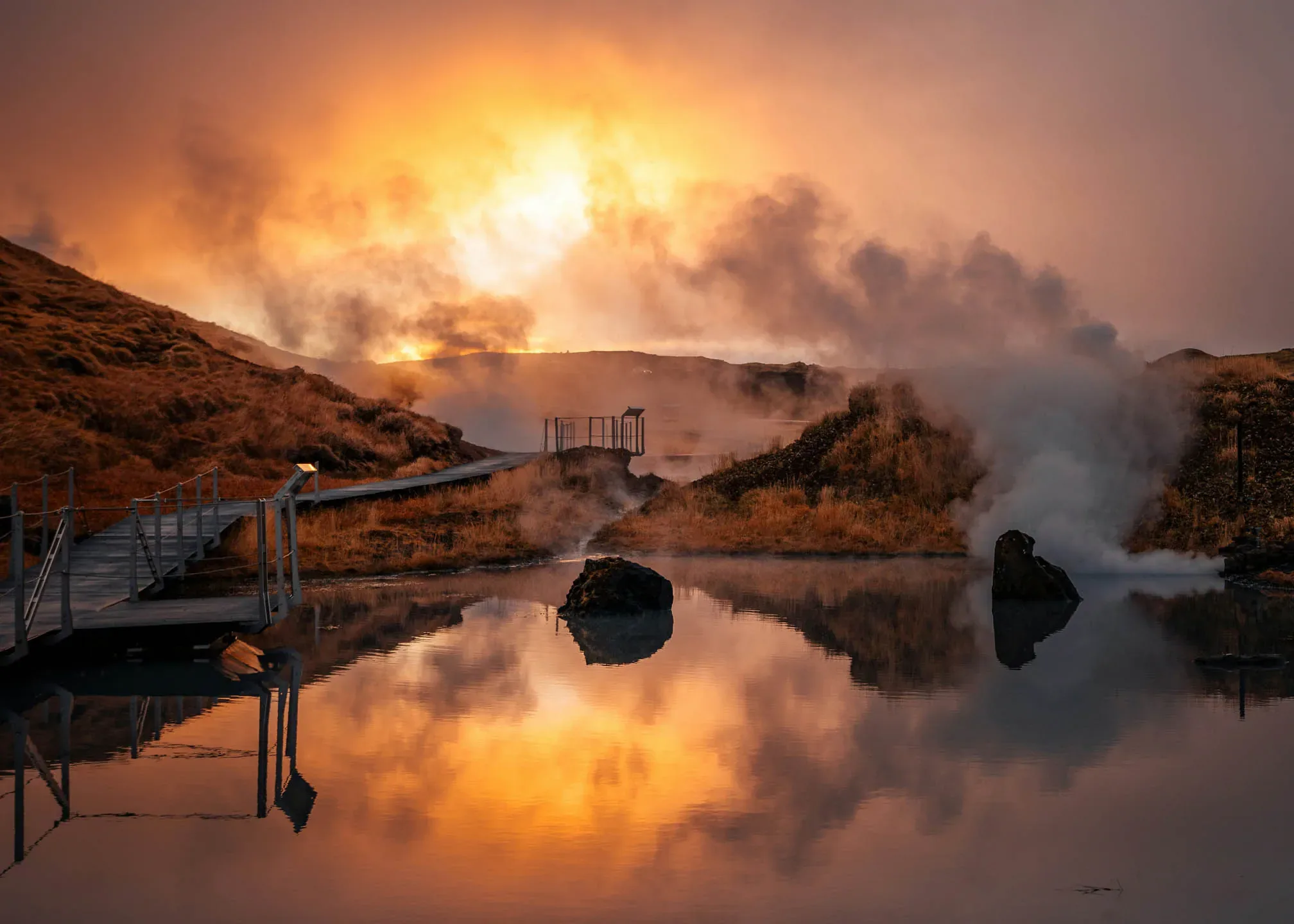 Geothermal hot spring in Iceland at sunset with rising steam and a wooden boardwalk