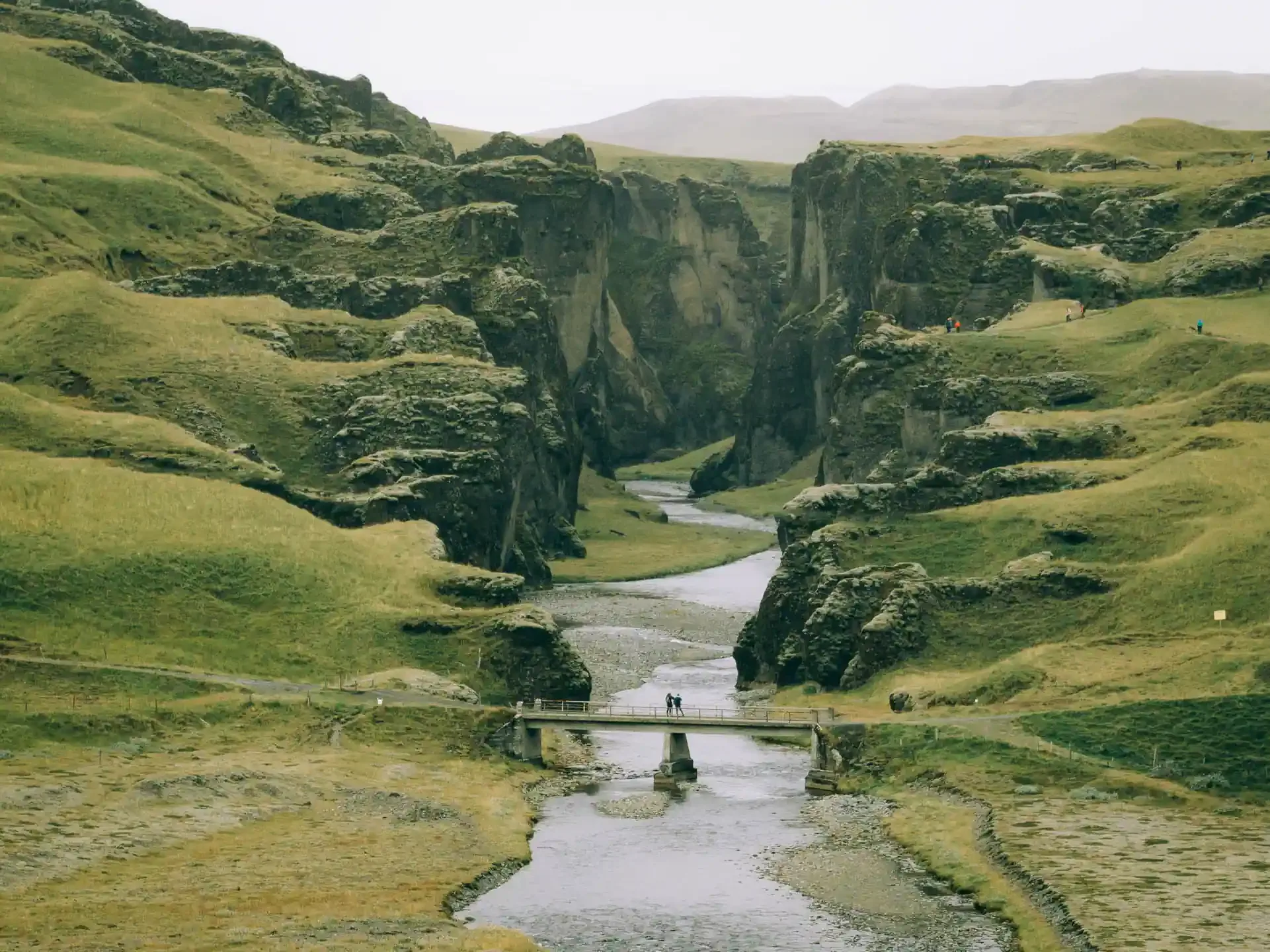 Bridge crossing a river through a dramatic green canyon in Iceland on a campervan travel route
