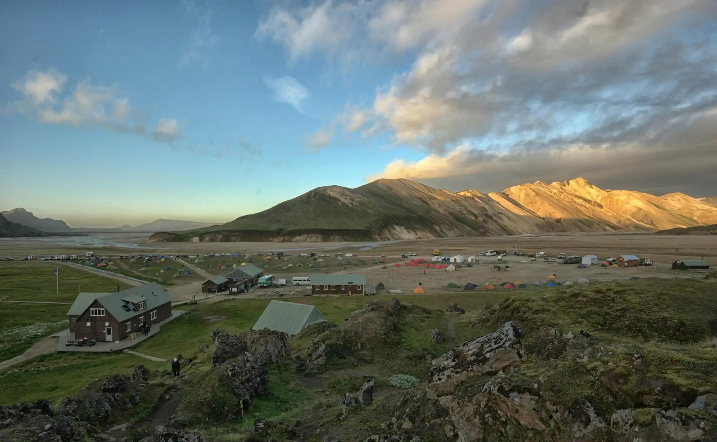 Cars campers and cabins at an Iceland campsite surrounded by green mountains