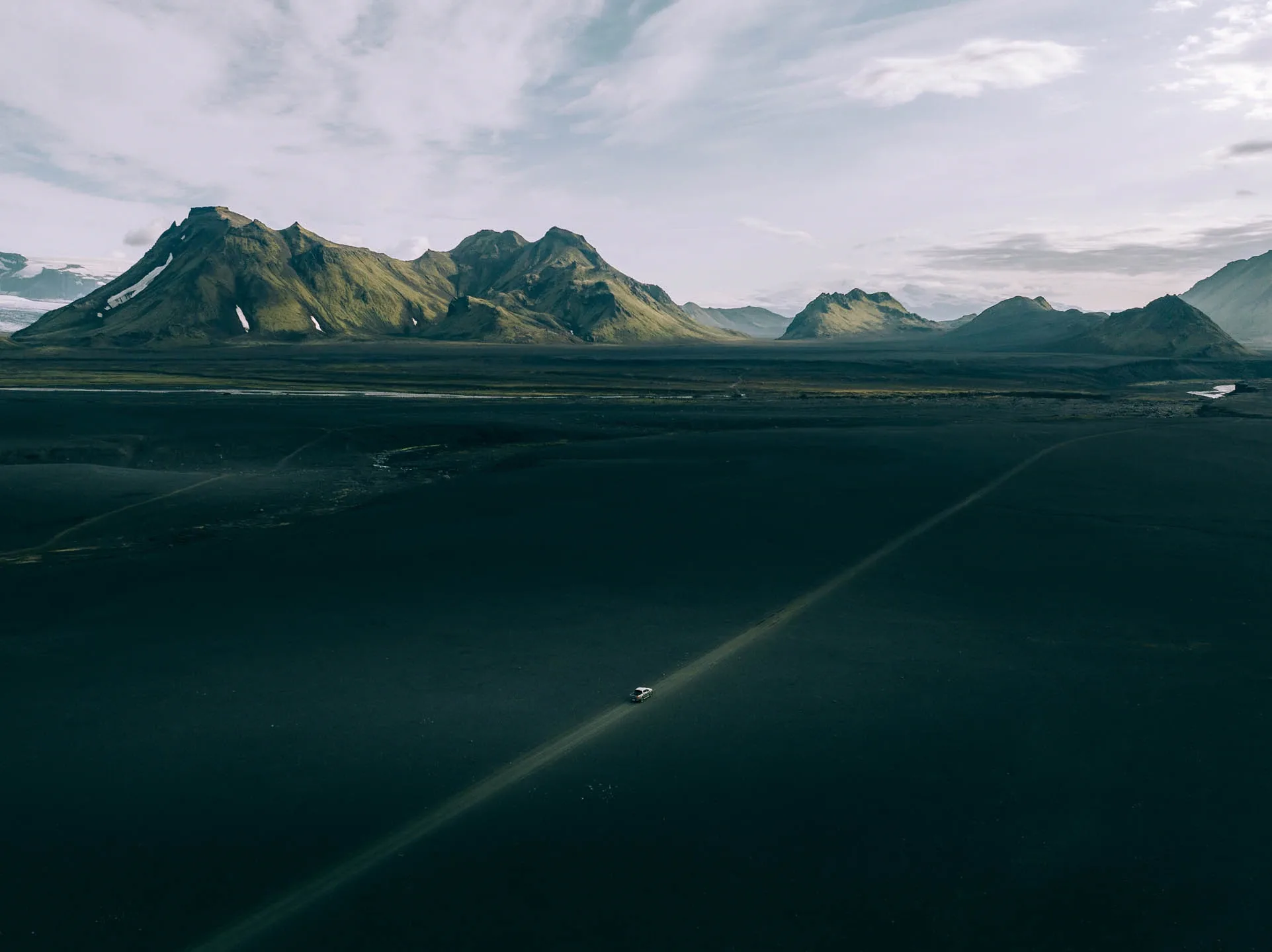 campervan travel Iceland driving along a remote gravel road across a vast black volcanic plain with green mountains and glacier peaks in the background in Iceland