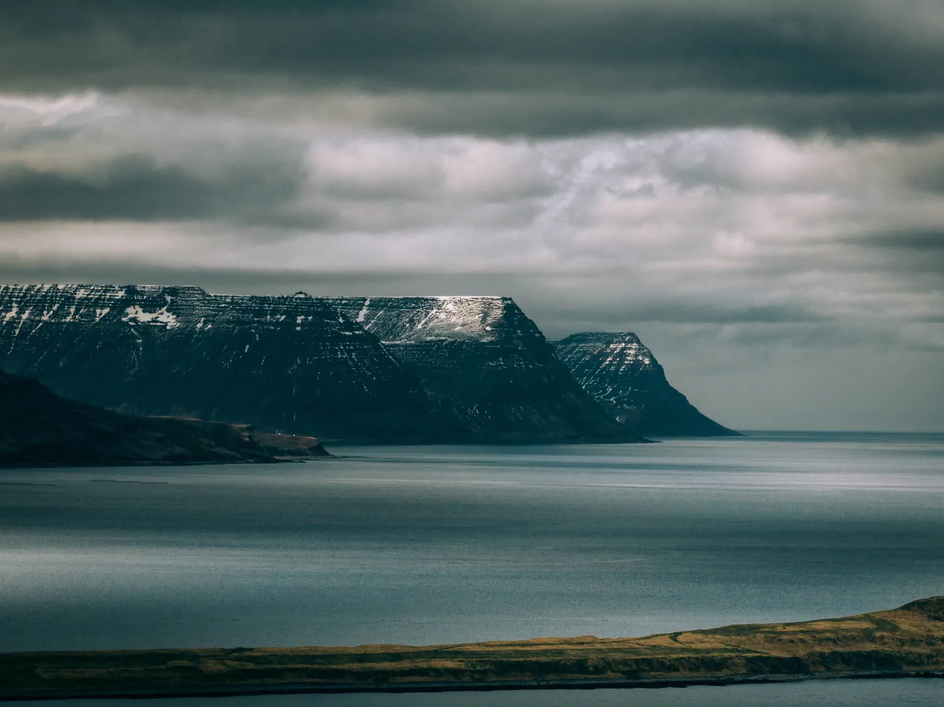 Dramatic fjords and snow-capped mountains overlooking the ocean in Iceland's remote Westfjords under a moody sky.