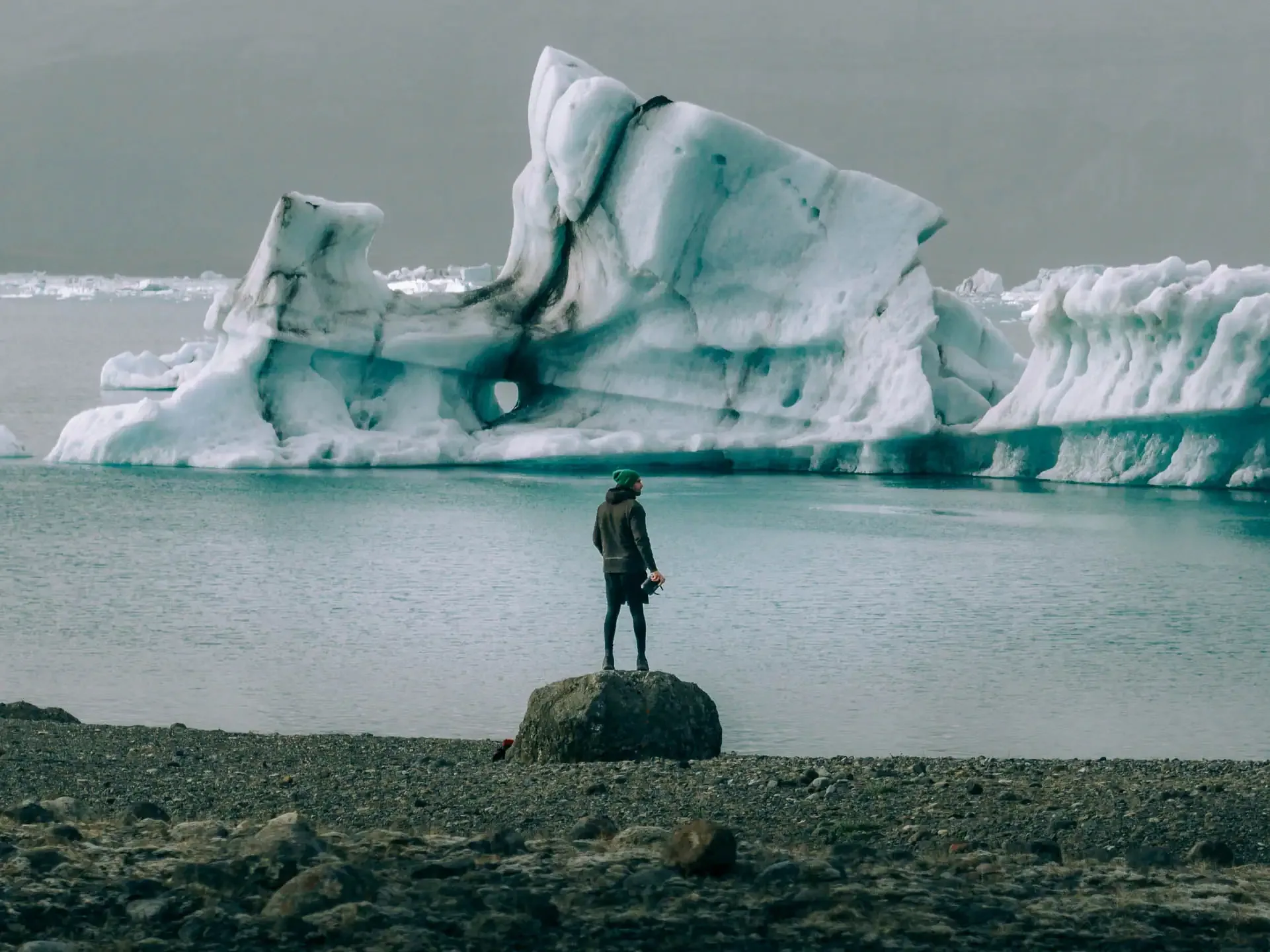 Person standing on a rock facing a floating iceberg at Jökulsárlón glacial lagoon in Iceland