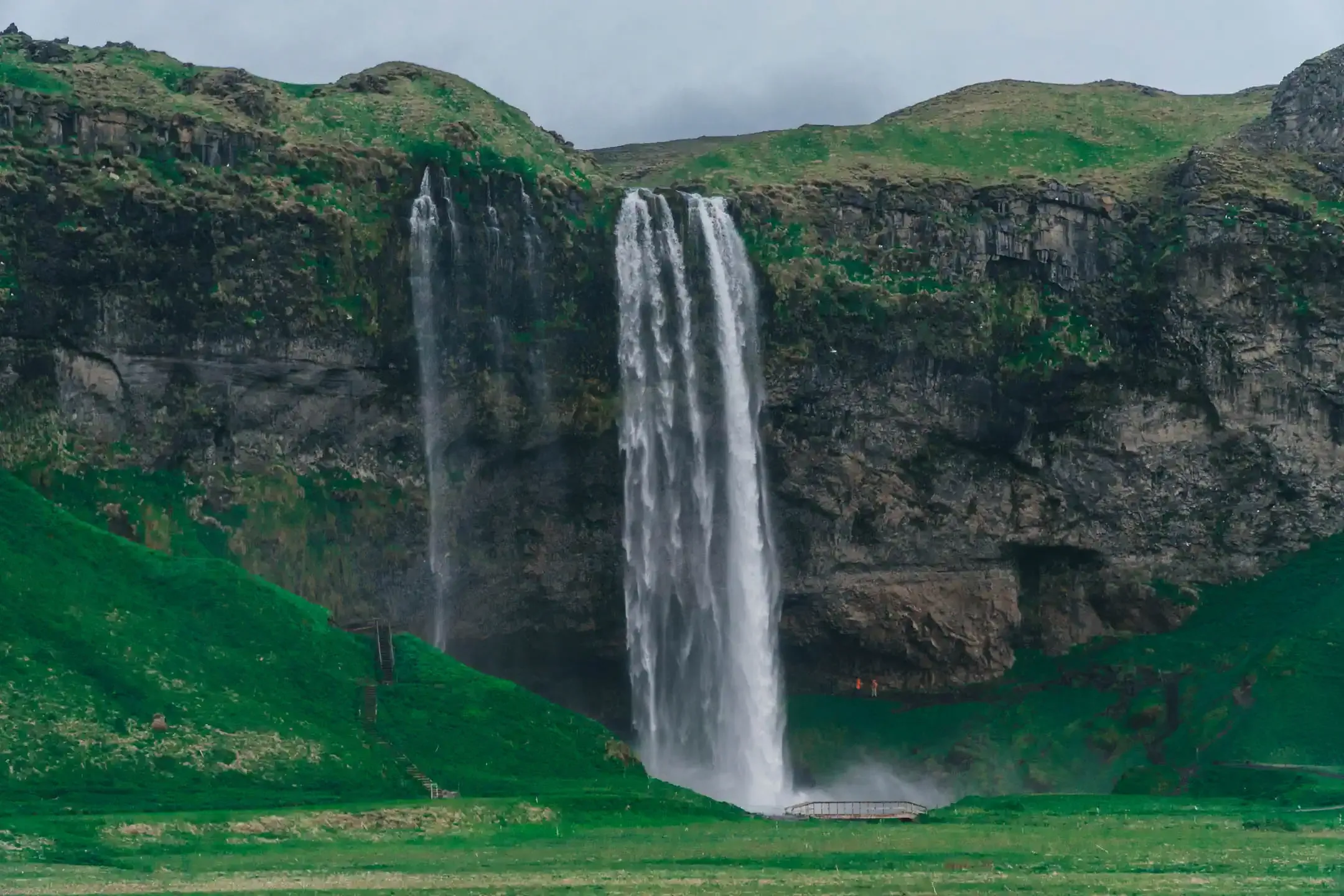 Seljalandsfoss waterfall cascading over a high cliff with lush green hills and walking path in South Iceland during a scenic campervan road trip