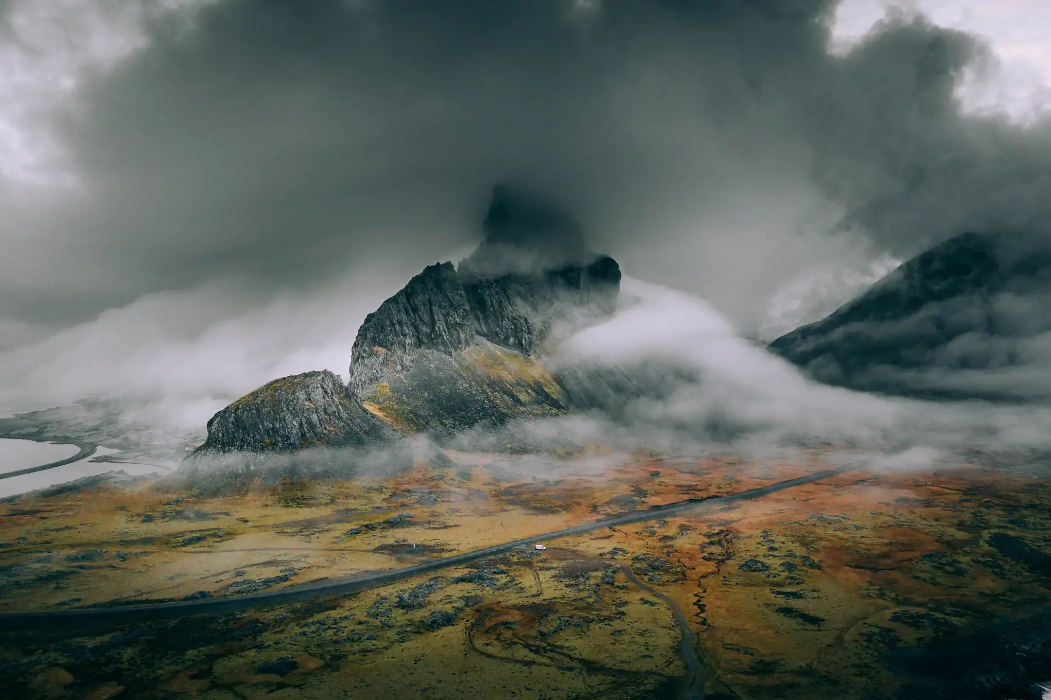 Dramatic mountain peaks covered in low clouds and mist along a remote road in Iceland.