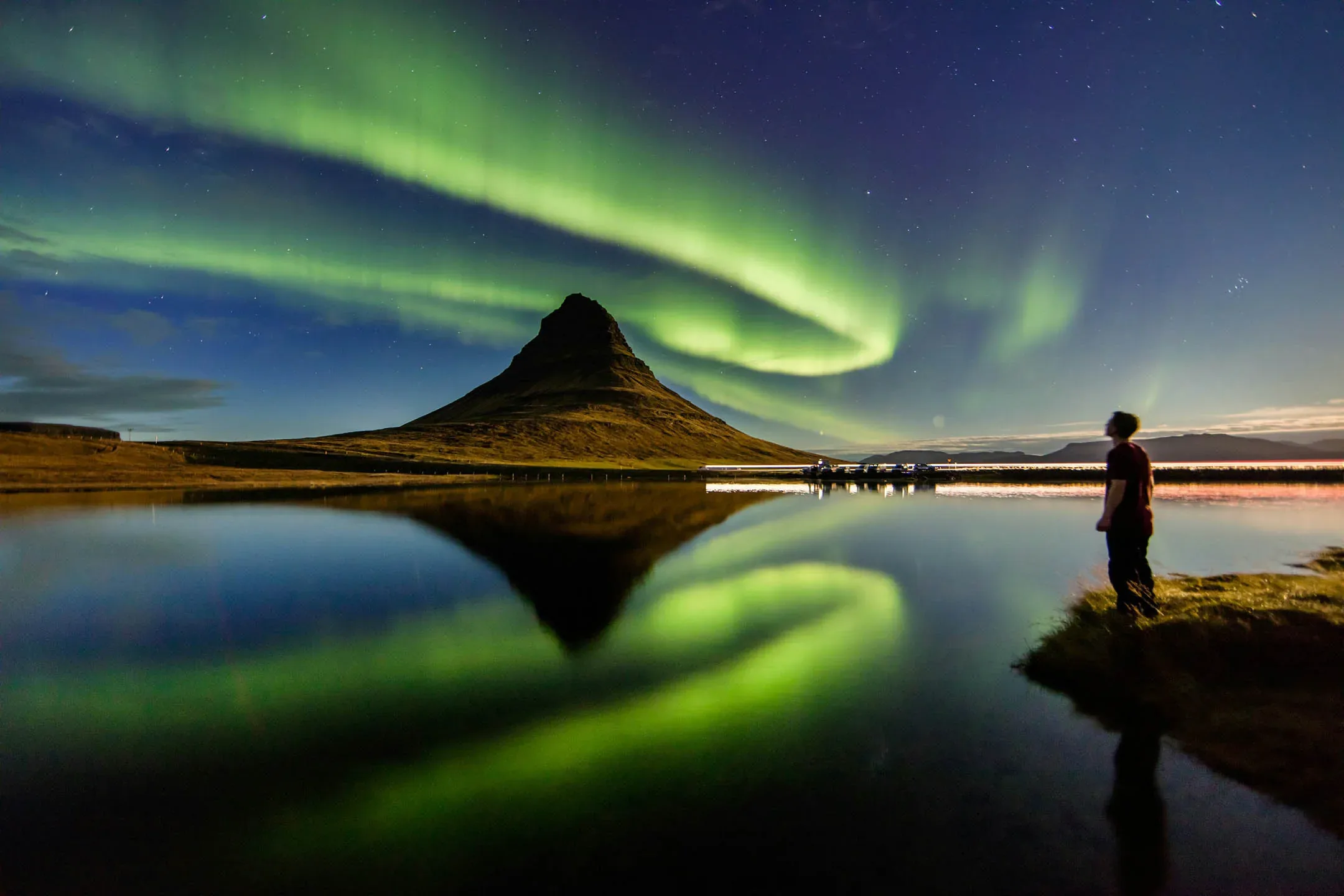 Northern Lights forming a green spiral above Kirkjufell mountain and its reflection in a calm Icelandic lake