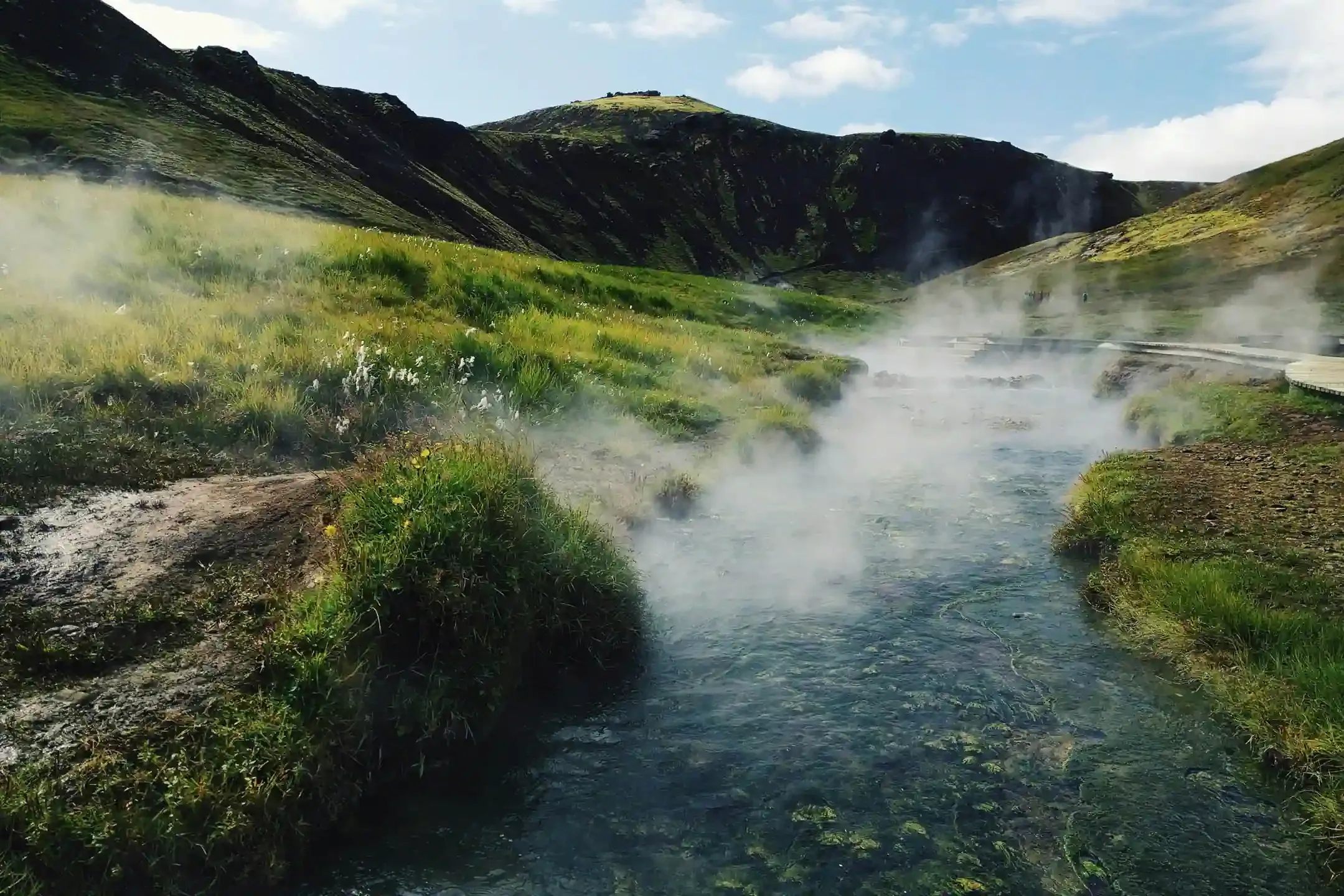 Reykjadalur hot spring river in Iceland with steam rising over green hills.