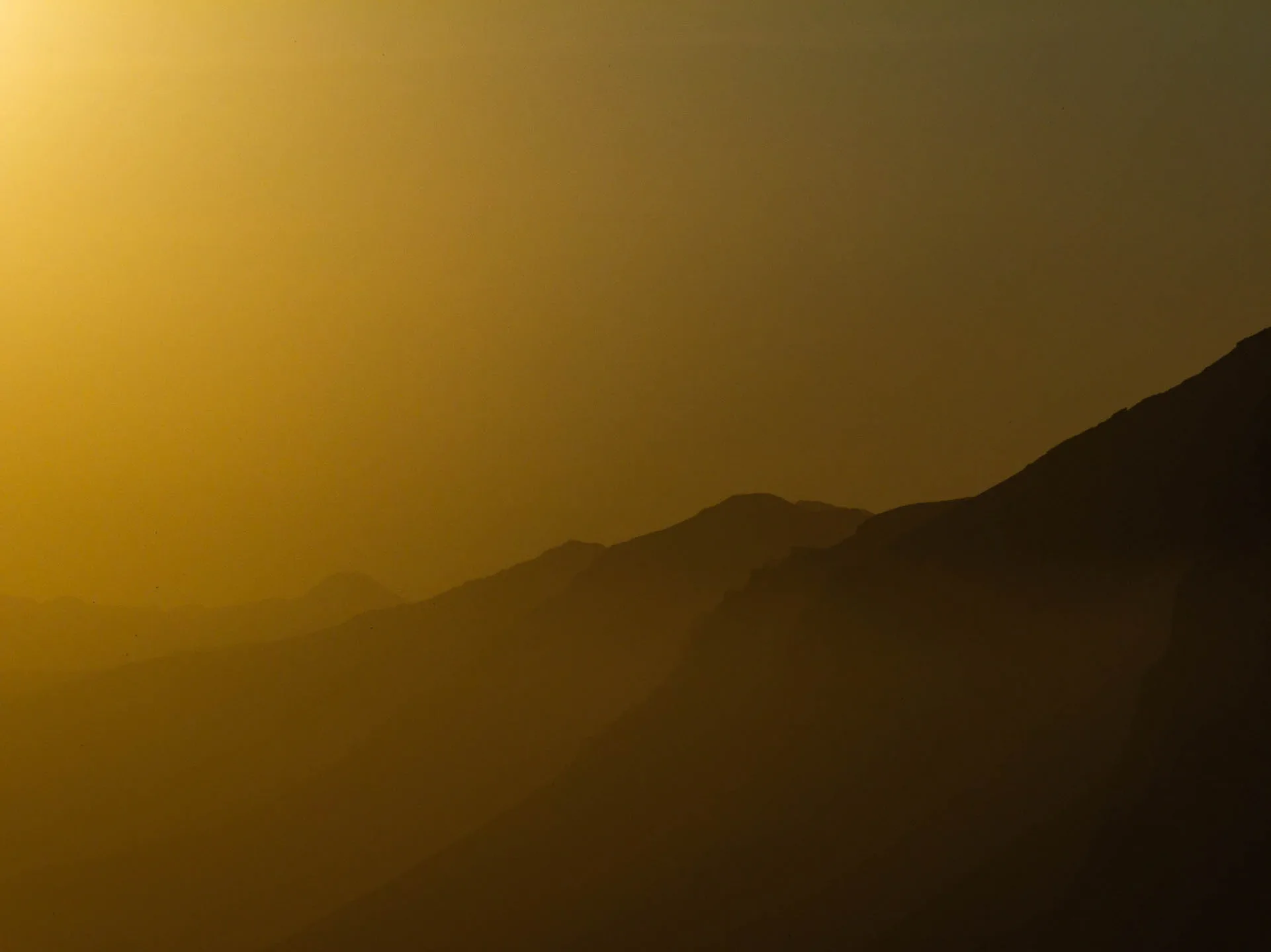 Golden sunset casting warm orange light over layered mountain ridges in Iceland, similar to the dramatic western skies expected during the 2026 solar eclipse.