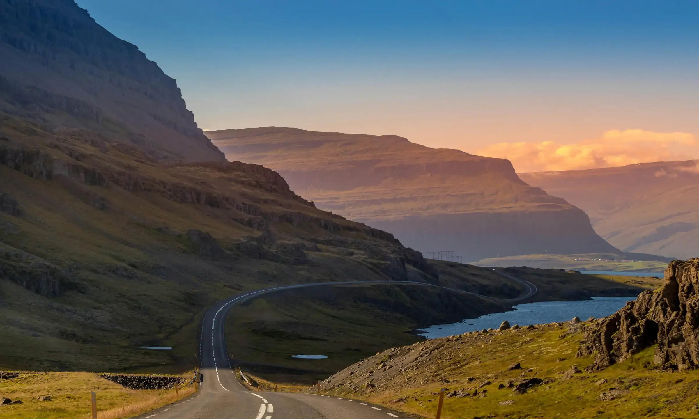 A scenic winding road through the Westfjords mountains at sunset, leading toward one of Iceland's best total eclipse viewing regions.
